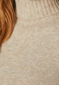 Beige stickad polotröja med en ribbad krage. Mjuk textur med ett subtilt mönster och varm, neutral ton.