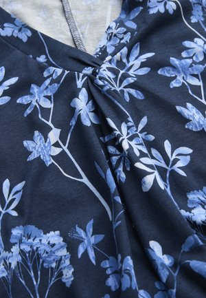 Dunkelblauer Stoff mit hellblauem und weißem Blumenmuster und einer zentralen gerafften Falte nahe einer Ausschnittnaht.