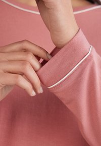 Roze langemouwshirt met een ronde hals, featuring witte piping langs de kraag en mouwmanchetten, met een zachte, gladde stoftextuur.