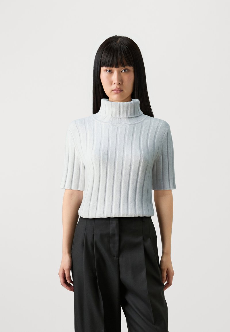 Hellgrauer, gerippter Rollkragenpullover aus weichem Material, mit kurzen Ärmeln und körpernahem Schnitt. Kombiniert mit taillierten schwarzen Hosen.