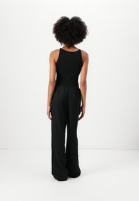 Top de alças preto com nervuras combinado com umas calças largas pretas, apresentando uma cintura elástica e um corte descontraído. Vista traseira contra um fundo simples.