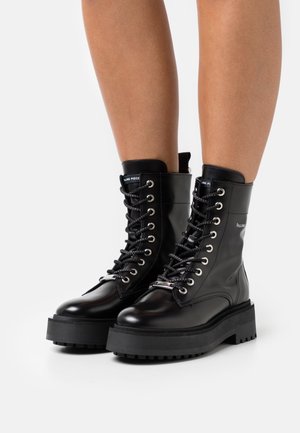 Stivali da combattimento in pelle nera con suola piattaforma spessa e lacci texture. Dotati di ferrature argentate e logo sulla caviglia.