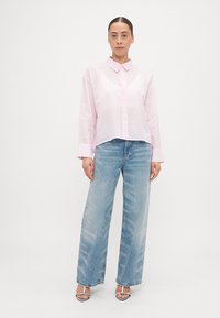 Light pink collared shirt with subtle dot pattern, paired with high-waisted blue jeans featuring a faded wash and wide leg.