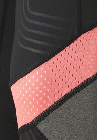 Černá sportovní tkanina s texturovaným vzorem, doplněná růžovou perforovanou částí a šedými detaily, s černým prošíváním.