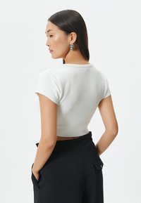 Hvid cropped top med korte ærmer, glat tekstur og rund udskæring, parret med højtaljet sorte bukser med sidelommer.