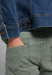 Jeansjacka i mörkblått med knäppningar och kontrasterande sömmar; matchad med ljusgröna byxor med sidofickor och strukturerad tyg.