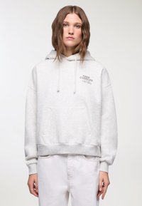 Felpa grigia chiaro realizzata in tessuto morbido, con tasca frontale, polsini a coste e una stampa "FREE CUDDLES" con un numero di telefono.