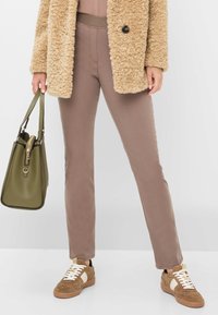 Beige, fluffy frakke, taupe tætsiddende bukser og brune sneakers. Oliven grøn taske med lynlås og struktureret design. Simpelt, afslappet outfit.