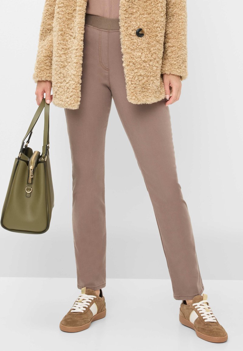Beige, fluffy frakke, taupe tætsiddende bukser og brune sneakers. Oliven grøn taske med lynlås og struktureret design. Simpelt, afslappet outfit.