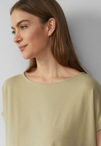 Korte mouw, lichtbeige top met een brede, ronde halslijn en een gladde textuur, die zachtjes over de schouders valt. Eenvoudig en veelzijdig ontwerp.