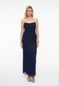 Námořnická strapless róba s detailními korálky a květinovými vzory, s dlouhou sukní a průsvitnou vrstvou. Stříbrné sandály na řemínky.