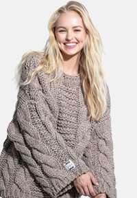 Gruby sweter z grubym splotem w jasnym odcieniu taupe, z szerokimi rękawami i prążkowanym dekoltem. Zawiera małą metkę marki na mankiecie.