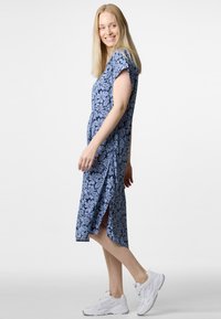 Kukallinen, polveen ulottuva mekko sinisen sävyissä, lyhyet hihat, sivuaukot, pehmeä kangas rentoa istuvuutta varten, yhdistetty valkoisiin lenkkareihin.