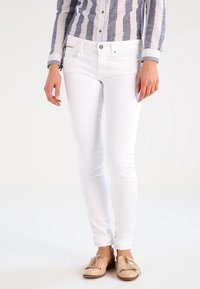 Vita smala jeans med en slät yta, traditionell femfickdesign och en enkel knappstängning. I kombination med bruna loafers med fransar.