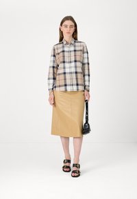 Karierte Button-Down-Bluse in Beige, Marineblau und Rot, kombiniert mit einem cremefarbenen, ledernen Bleistiftrock. Schwarze Sandalen mit Schnallen und einer kleinen schwarzen Handtasche.