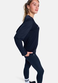Lange mouwen sporttop in donker marineblauw, gemaakt van lichtgewicht stof, gecombineerd met strakke marineblauwe leggings en gestreepte enkelsokken.