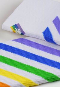 Zwei Handtücher: eines weiß mit einem Regenbogen-Tag, das andere mit bunten Streifen in Blau, Grün, Gelb und Lila auf einer strukturierten Oberfläche.