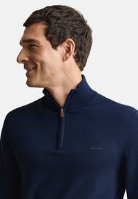 Marineblauwe trui met een ritssluiting bij de kraag, gemaakt van zachte stof. Heeft een subtiel merkembleem op de borst en een gladde textuur.