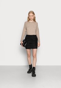 Maglione beige lavorato a maglia, gonna mini in suede nera e stivaletti neri con fibbie. La borsa è nera con un dettaglio arricciato.