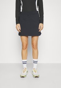 Černá sukně z jerseye s hladkým povrchem, midi délka a nenápadný pas, doplněná bílými ponožkami se modrými pruhy a teniskami.