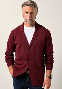 Burgundy kavaj med en enkel ficka, spetsig krage och framknappar; texturerad tyg med långa ärmar, bärs över en vit skjorta.