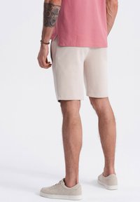 Shorts en coton beiges avec poches latérales, présentant une texture lisse et une coupe à mi-genoux, associés à des baskets beige clair.