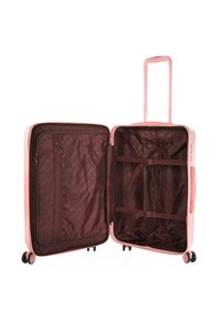 Maleta dura rosa con doble cremallera, mango retráctil y cuatro ruedas. El interior cuenta con un forro de tela marrón y correas cruzadas.