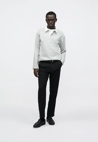 Szara polo z długim rękawem i białym kołnierzykiem, zestawiona z czarnymi spodniami i czarnymi butami, tworząca monochromatyczną stylizację.