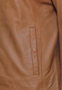 Braune Lederjacke mit einer glatten Textur, genähten N�ähten und einer horizontalen Tasche. Die Farbe ist ein warmes, reichhaltiges Tan.
