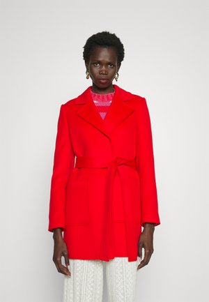 Red wool blend coat with notch lapels, belted waist, and two front pockets. Model wears a pink knit sweater underneath.
