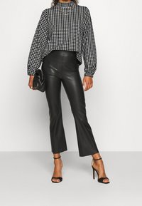 Haut à motif pied-de-poule noir et blanc avec des manches bouffantes, associé à un pantalon évasé en simili cuir noir taille haute et des talons noirs.