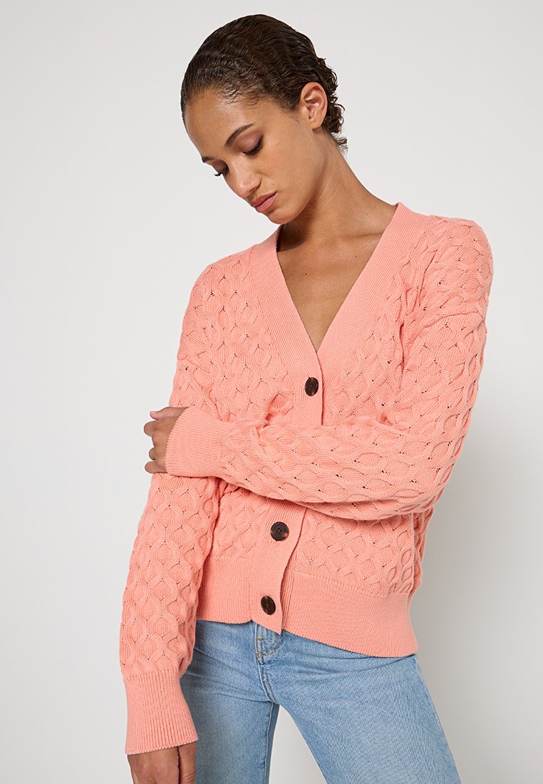 Różowy dziergany kardigan z fakturowanym wzorem diamentowym, z dekoltem w serek i ciemnymi guzikami. Długie rękawy z prążkowanymi mankietami i dół.
