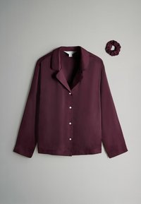 Blusa de seda burdeos con cuello muesca, mangas largas y cierre de botones; incluye una coleta de tela a juego. Textura suave, diseño minimalista.