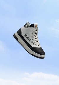 Basket montante avec des panneaux blancs et noirs, des lacets blancs, un marquage Moschino sur le côté et un logo ourson sur la languette sur fond de ciel bleu.