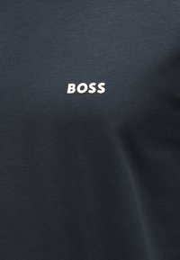 Μαύρο ύφασμα με τη λέξη "BOSS" τυπωμένη σε λευκό, κεντραρισμένη και με έντονα κεφαλαία γράμματα.