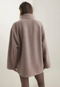 Veste en polaire beige surdimensionnée, avec un col montant, un tissu texturé et des manches amples. Pas de fermetures ni d'accents visibles.