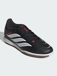 Μαύρο εσωτερικό παπούτσι ποδοσφαίρου Adidas Predator με λευκές ρίγες, κόκκινες λεπτομέρειες και καφέ σόλα σε ανοιχτό φόντο.