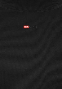 Schwarzer, gerippter Rollkragenpullover mit schlanker Passform, versehen mit einem kleinen roten und weißen Diesel-Logo auf der Brust. Glatte Textur und hoher Kragen.