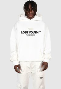 Fehér kapucnis pulóver, melyen fekete színnel a "LOST YOUTH" és a "Cooperations" felirat látható. Elöl zsebbel rendelkezik és laza szabása van. Fehér nadrággal párosítva.