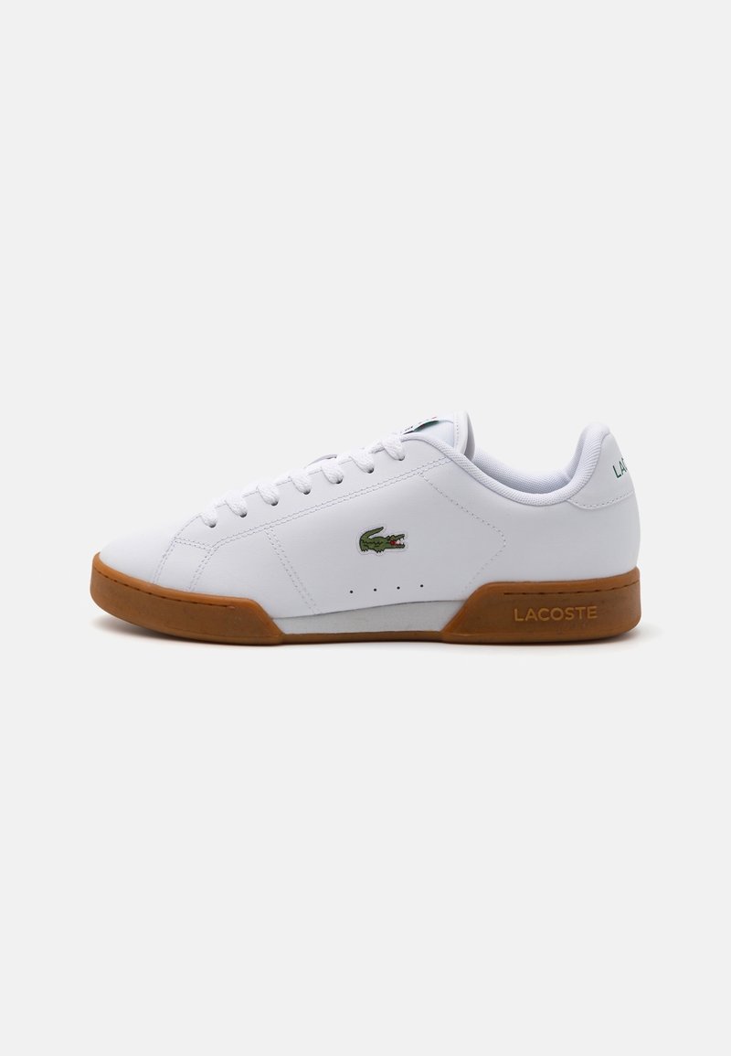 Baskets blanches Lacoste avec semelle marron, logo crocodile vert sur le côté et texte "Lacoste" embossé sur la semelle du talon.