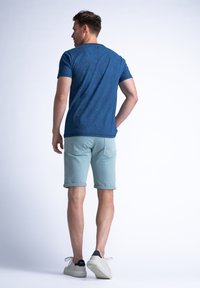 Una camiseta azul marino con un patrón sutil se combina con pantalones cortos de color azul claro. Los pantalones cortos tienen dobladillos enrollados y bolsillos traseros. Unas zapatillas blancas completan el look.