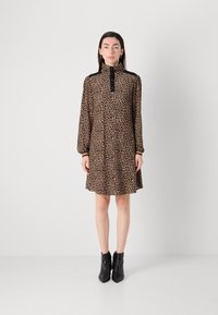 Kleid mit Leopardenmuster, langen Ärmeln, hohem Kragen, geknöpften Verschluss und schwarzen Akzenten. Kombiniert mit schwarzen Stiefeletten. Glatte Stoffstruktur.
