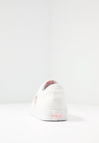 Vit kanvas sneakers med rosa detaljer på hälfliken och sidan. Platt sula med texturerat material, med en logga på baksidan.