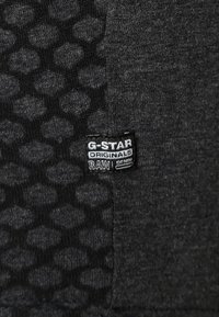 Tissu noir avec un motif en nid d'abeille texturé et une étiquette cousue portant "G-STAR ORIGINALS RAW DENIM."