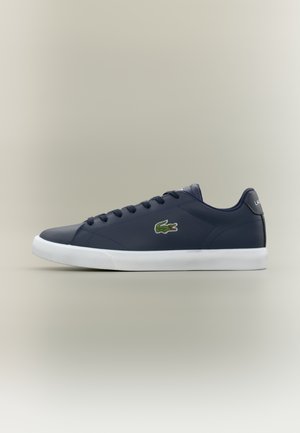 Sötétkék alacsony szárú sneaker fehér talppal, fűzős elejével és zöld krokodil logóval az oldalán.