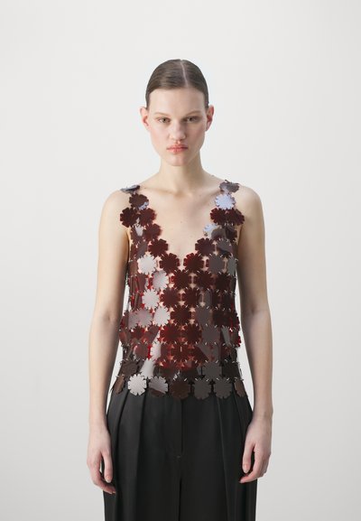 Red and silver floral-patterned sleeveless top made of metallic material, featuring a deep V-neck and layered design, worn with black trousers.