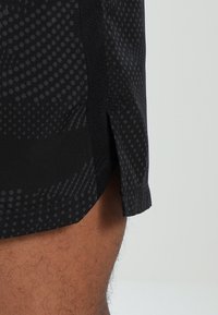 Svarta sportiga shorts med prickigt mönster, slät struktur och sidslitsar längst ner för bättre rörlighet.
