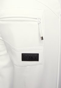 Witte stof met een gladde textuur, voorzien van een zwart patch met het label "ROXY" en een ritszak. Eenvoudig ontwerp met subtiele stiksels.