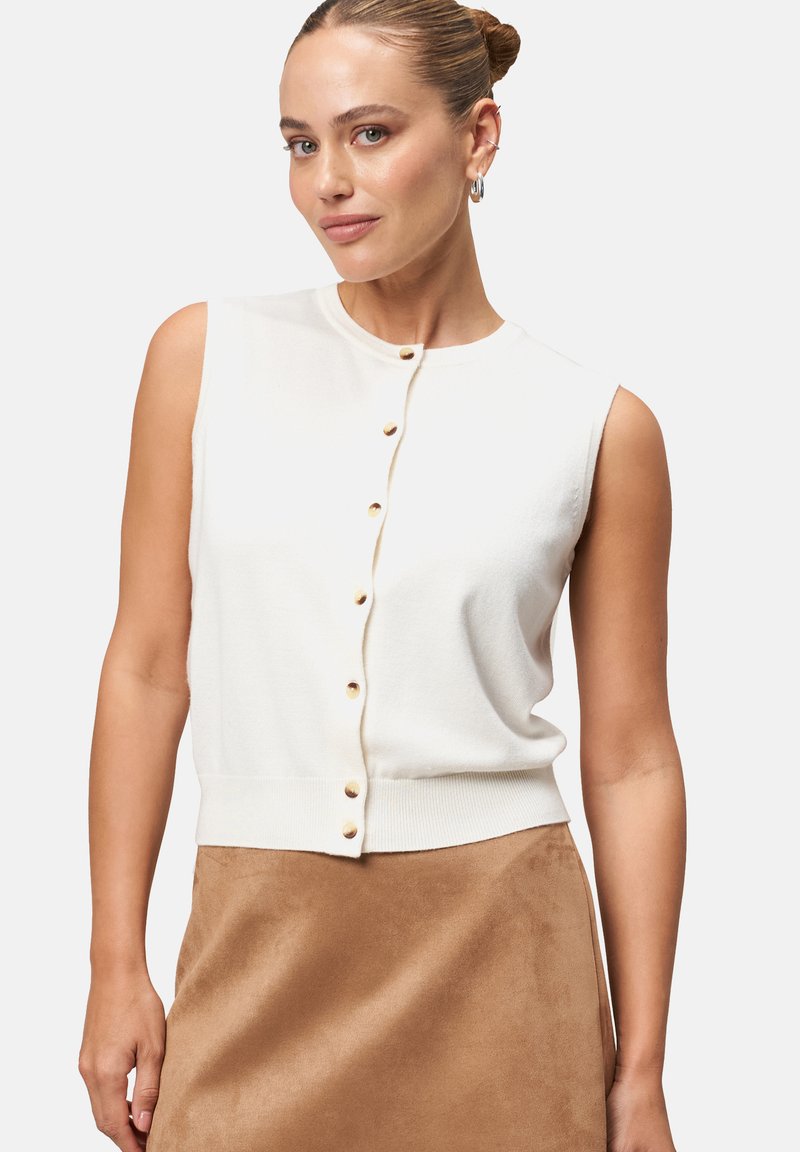 Pull blanc sans manches avec col rond, doté d'une rangée de boutons dorés sur le devant et d'un ourlet côtelé. Texture douce, design ajusté.