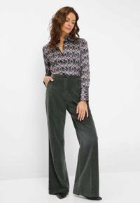 Chemise à manches longues avec col, ornée d'un motif coloré, associée à un pantalon large en velours côtelé vert. Tissu doux et coupe décontractée. Chaussures noires.